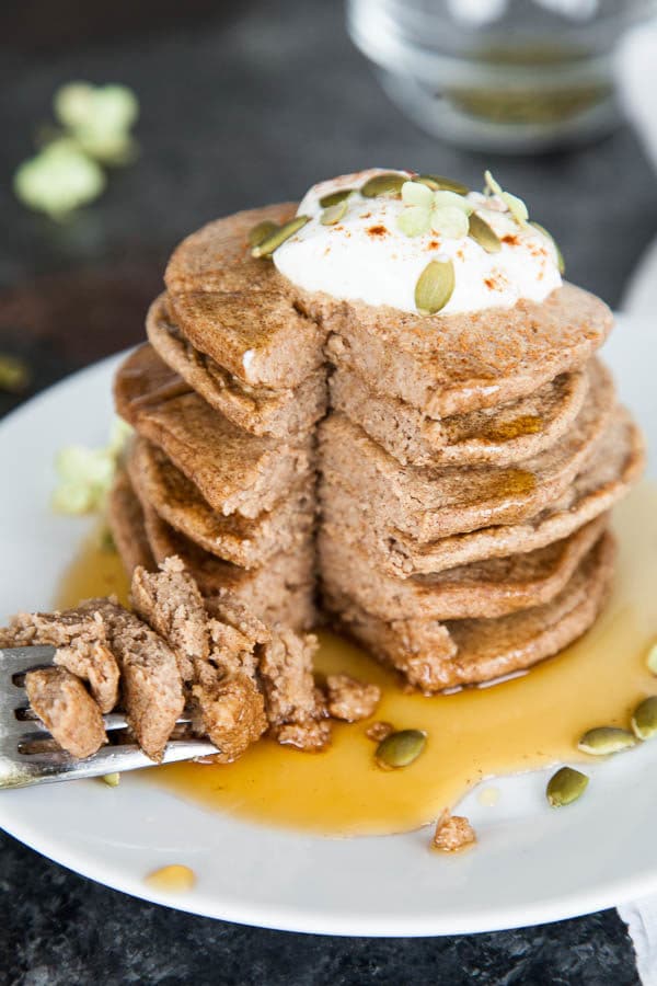 Stack of pancakes on a white plate with a fork taking a bite.