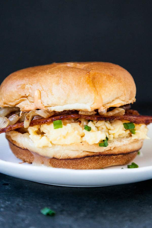 The Copycat Eggslut Sandwich is creamy scrambled eggs and chives inside a lightly toasted brioche bun, with cheddar cheese, caramelized onions, and sriracha mayo.