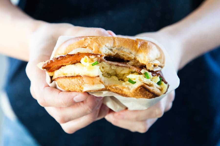 The Copycat Eggslut Sandwich is creamy scrambled eggs and chives inside a lightly toasted brioche bun, with cheddar cheese, caramelized onions, and sriracha mayo.