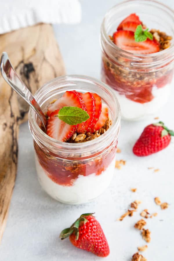 Breakfast parfaits with homemade strawberry rhubarb compote layered with Greek yogurt and granola. Recipe yields up to 6 half-pint mason jar servings - perfect for meal prepping!