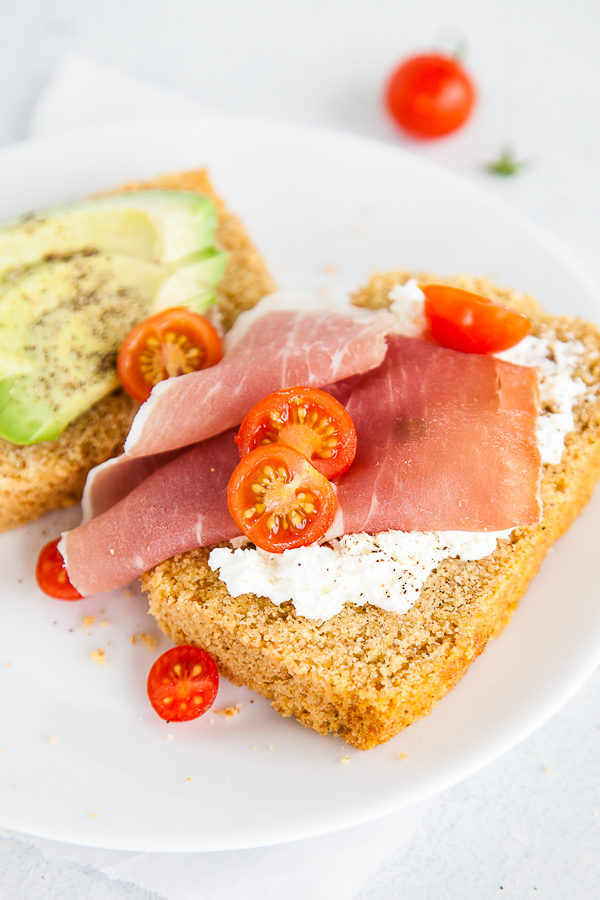 Slices of cornbread with prosciutto, tomatoes, and avocado on top.